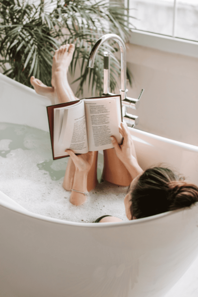 Richtig baden – So nutzen Sie die Vorteile eines Entspannungsbads optimal 2 Frau ein Buch lesend in Badewanne mit Füßen auf Rand